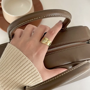 Polished wide gold ring styled on a model's hand with a brown leather handbag bag