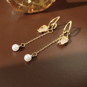 Détail de boucles d'oreilles tulipe à pompons avec perles et touches dorées sur cuir