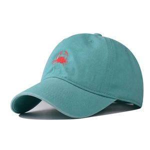 Detailed close-up of a teal blue baseball cap featuring a red crab embroidery on the front