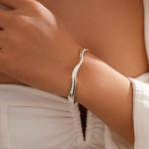 Close-up of minimalist wave-shaped silver bangle showing smooth fluid design on wrist