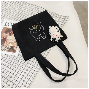 Detail of black corduroy tote bag featuring rabbit embroidery and a plush cow charm