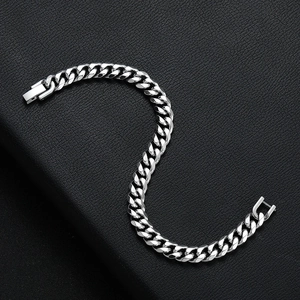 Detailed close-up of a silver Cuban link chain bracelet on a black leather background