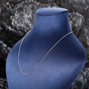 Detail shot of a delicate silver chain necklace displayed on a navy blue velvet mannequin