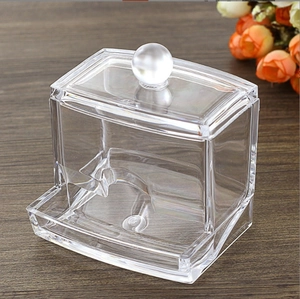 Clear acrylic storage box for cotton pads with a round handle lid on a dark wood surface