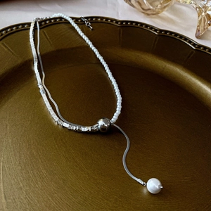 Close-up of double-layer silver chain and pearl necklace with heart pendant detail