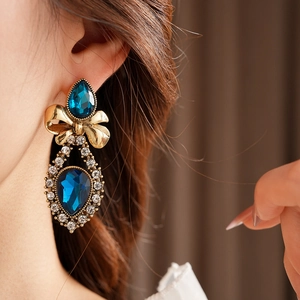 Close-up of vintage gold bow earrings with blue teardrop crystals worn by a model