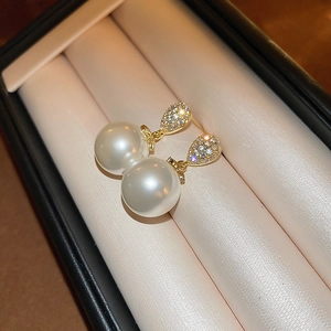 Elegant gold drop earrings with white pearls and sparkling zircon on satin background