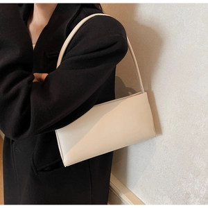 Close-up of white leather shoulder bag styled with a dark coat on a fashion model