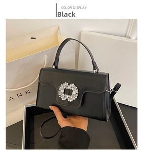 Detalle del bolso bandolera negro con hebilla de cristal frente al empaque de regalo