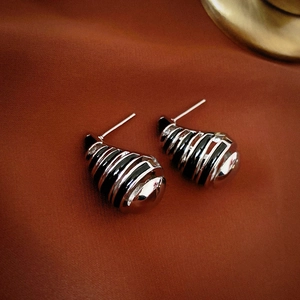 Detailed view of silver-tone spiral stud earrings with black drip oil stripes on clay fabric