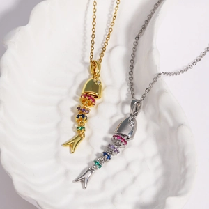 Detail view of gold and silver fishbone pendants with colorful stones in a shell dish