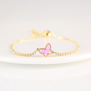 Macro detail of a golden butterfly bracelet featuring pink charm and white crystals