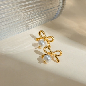 Detail view of 18K gold bow knot earrings with white round pearls on a textured background