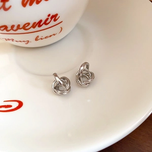 Close-up of silver minimalist twisted hoop earrings on a white ceramic tray