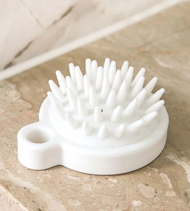Detail view of white silicone scalp massager brush on a marble surface with handheld design
