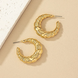 Macro shot of gold-plated croissant-style C-shaped hoop earrings with a twisted texture