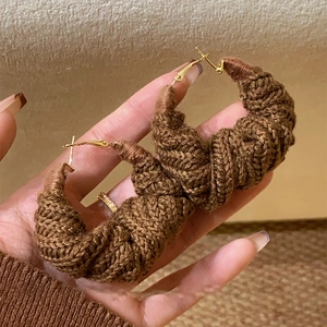 Brown crochet knit hoop earrings with gold metal clasp on a minimalist warm background