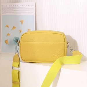 Detailed macro of yellow litchi-grain leather texture with wide fabric strap and silver hardware