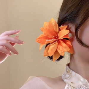Detail of a large orange fabric lily hair clip worn with elegant pearl earrings