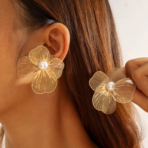 Détail de grandes boucles d'oreilles fleur dorées avec texture tissée et perle blanche
