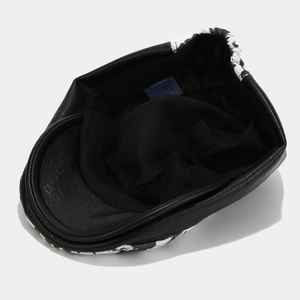 Detail view of the black PU leather brim and woven brand label inside the retro newsboy cap
