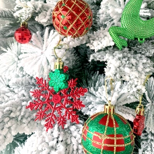 Dettaglio di ornamenti natalizi rossi, verdi e dorati appesi a un albero innevato