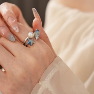 Macro detail of conch and pearl open ring with blue enamel on a model's finger