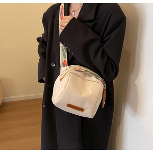 Detail of canvas shell bag with colorful wide strap and leather trim on black coat