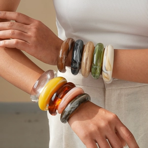 Stack of colorful acrylic geometric cuff bracelets in amber and marble textures on model arm