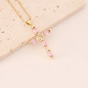 Close-up of gold cross necklace with pink zircon crystals on a stone background