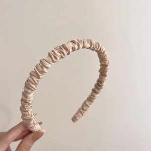 Detail of champagne gold satin pleated headband with elegant ruffled texture and silk gloss