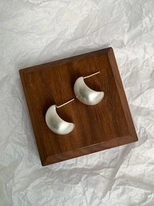 Close-up of matte silver C-shaped geometric earrings on a minimalist wooden display stand