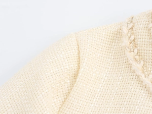 Vista dettagliata del tessuto tweed beige con fili dorati e finitura intrecciata sul collo