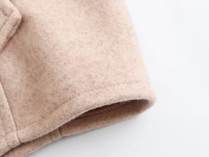 Detailaufnahme der beigen Wollstofftextur und der sauberen Nähte an einem kurzen Mantel