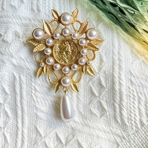 Detail of vintage matte gold brooch with leaf motifs, pearl accents and a portrait coin