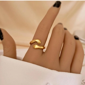Detailed macro shot of a gold embrace hands ring worn on a finger with a warm fabric backdrop