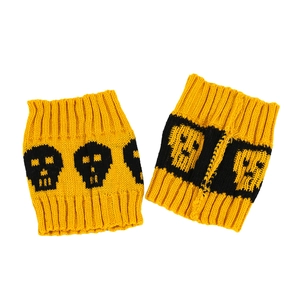 Macro view of knitted yellow leg warmers featuring black skull patterns on white background