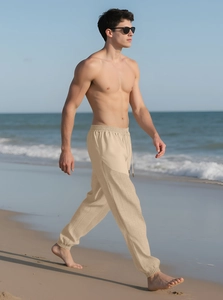 Men's khaki drawstring linen trousers shown in a breezy beach setting with a loose fit
