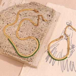Detailed close-up of 18K gold snake chain necklace with green zircon stones on stone base