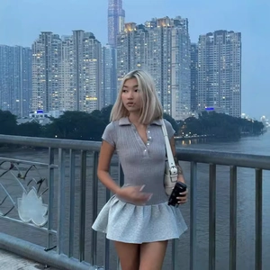 Robe polo en maille grise avec jupe plissée portée par un mannequin sur un pont de ville