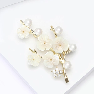 Élégante broche fleur de prunier dorée avec perle et pétales en nacre sur un support