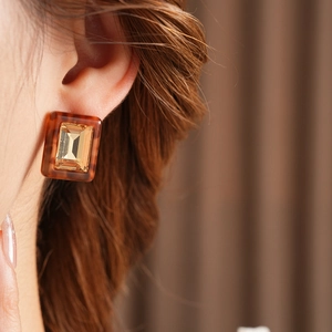 Close-up of amber resin square earrings with golden center gemstone on female model
