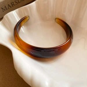Detail view of a vintage dark brown resin bangle with amber texture on a ceramic dish