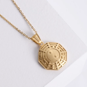 Golden Tai Chi Yin Yang pendant necklace made of stainless steel on white pedestal