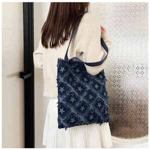Deep blue denim tote bag with white star patterns and frayed edges on a model