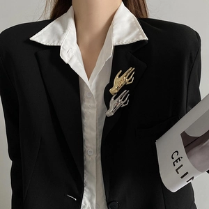 Close-up of golden hand-shaped brooch on black suit lapel with metallic finish