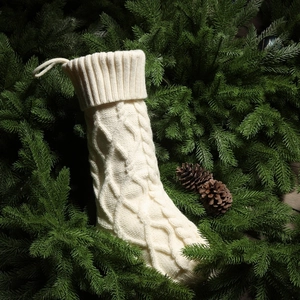 Detailed view of white knitted Christmas stocking with diamond cable patterns on pine branches
