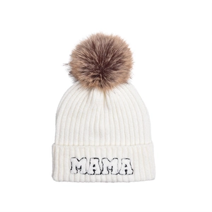 Detail of white knit beanie featuring MAMA embroidery and a faux fur pompom ball