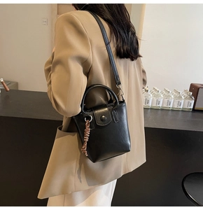 Close-up of a black leather crossbody bag with adjustable strap and woven charm detail