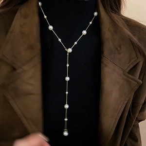 Detailed view of elegant Y-shaped long pearl necklace styled on a black turtleneck sweater